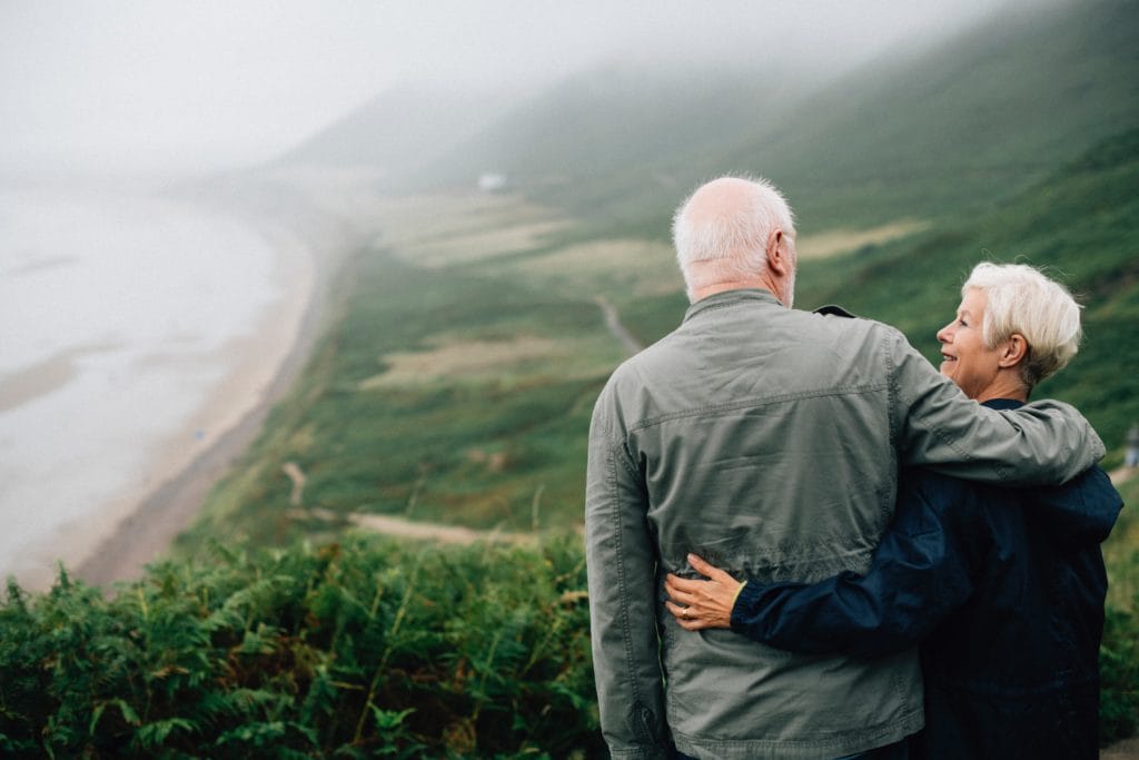 Elderly couple stand together at scenic overlook.